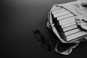 foto preto e branco de livros e óculos sobre fundo neutro escuro, com espaço livre para texto,...