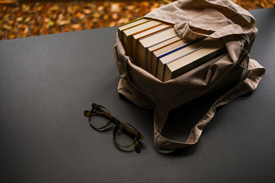 Foto de ângulo superior com livros dentro de bolsa em fundo neutro escuro com folhas de outono. óculos para leitura. ninguém. espaço livre para texto.