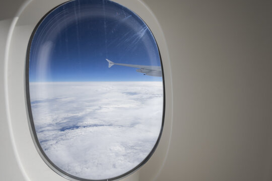 View of a plane's wing slicing through fluffy white clouds beneath a clear blue sky seen from an airplane window, Christchurch, Canterbury Region, New Zealand.