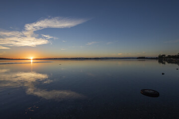 View of the serene water reflecting the warm glow of the setting sun beneath a blue sky dotted with soft clouds, Christchurch, Canterbury Region, New Zealand.