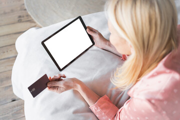 Top view of mockup image of a woman holding tablet with blank desktop white screen and credit card laying on bed at home making online shopping order purchasing on Internet E-commerce subscription