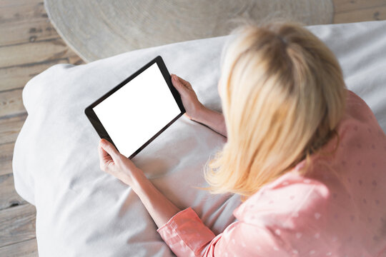 Mockup image of a woman holding tablet with blank desktop white screen laying on bed at home for social media or streaming subscription app video online shopping website with middle age female person