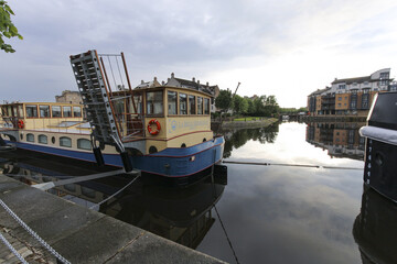 Edinburgh, United Kingdom - 23 June 2016: View of a canal boat with a raised ramp, reflecting the muted sky and nearby buildings in the calm water.