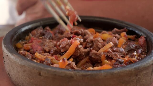 Person eats meat and vegetable stew baked in clay pot close-up