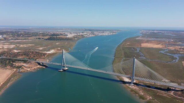 Cable-stayed Guadiana International Bridge connecting Spain and Portugal over wide river viewed from above on sunny day with green wetlands. Concept of cross-border infrastructure and European unity