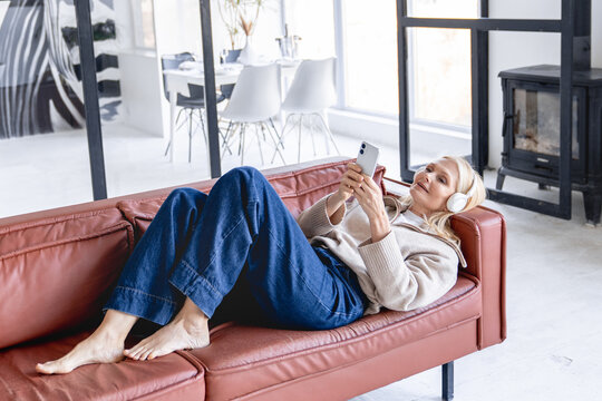 Enjoying music. Portrait smiling mature woman wear digital headphones recline on sofa listen to songs from chosen playlist with closed eyes chill relax catching meditative sounds online on cellphone