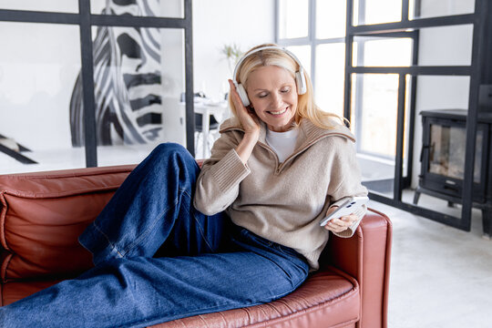 Headphones, mature woman and cellphone for music in home, listen and song in living room. Joyful, lounge and online audio streaming for sing along app, karaoke and games for female person on sofa