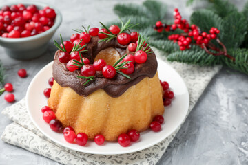 Delicious Christmas cake with chocolate glaze, cranberries and rosemary on light grey textured table, closeup