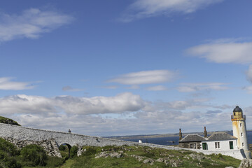 View of the lighthouse standing tall on the rocky coastline under the bright blue sky scattered with fluffy clouds, Isle of May, Scotland, United Kingdom.