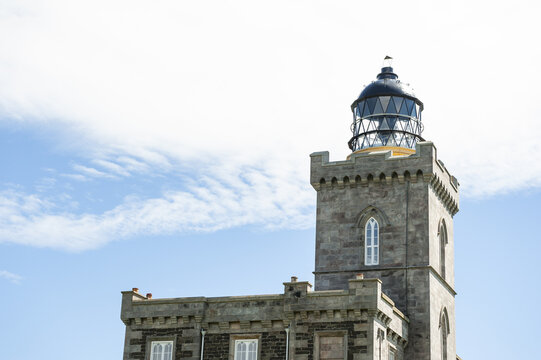 View of a majestic stone lighthouse stands tall against the backdrop of a bright blue sky dotted with wispy clouds, Isle of May, Scotland, United Kingdom.