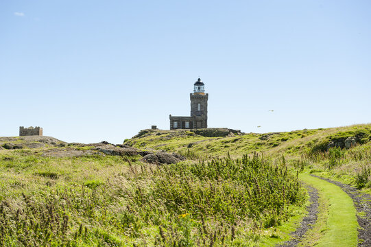 View of a weathered lighthouse stands sentinel atop a grassy hill, its sturdy grey stone contrasting with the vibrant green path, Isle of May, Scotland, United Kingdom.