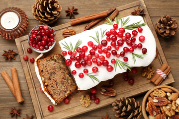 Tasty Christmas cake with icing, cranberries and rosemary on wooden table, flat lay