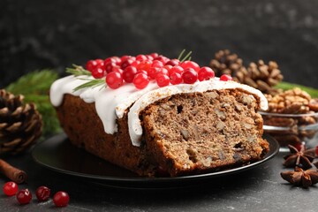 Tasty Christmas cake with icing, cranberries and festive decor on black table, closeup