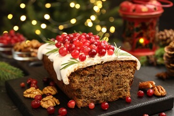 Tasty Christmas cake with icing, cranberries, nuts and festive decor on black table against blurred lights, closeup. Bokeh effect