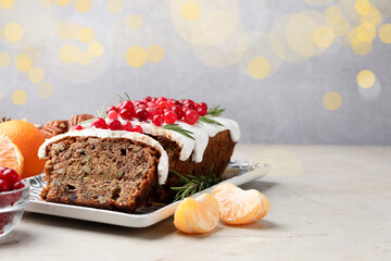 Tasty Christmas cake with icing, cranberries, nuts, tangerines and festive decor on light grey table against blurred lights, space for text. Bokeh effect