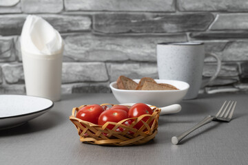 Fresh red tomatoes in a woven basket with snacks and drinks on a gray table in a cozy kitchen setting