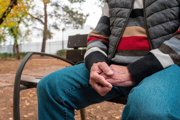 A close-up of an older man's hands resting on his lap while seated on a park bench, highlighting texture, age, and calmness.