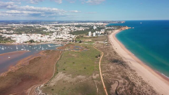 Alvor aerial view drone aerial coastline stretch with golden beach and turquoise sea, dune path and nearby golf greens leading to resort skyline, clear blue water edged by sandy shore, ideal