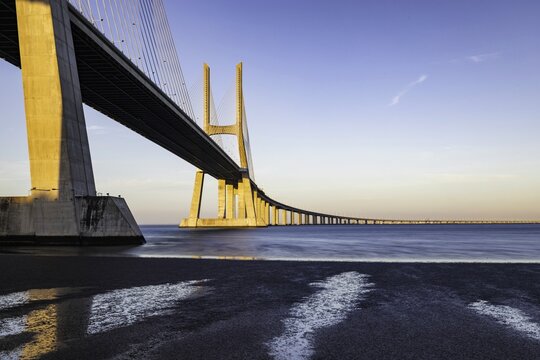 View of golden light bathing the colossal Vasco da Gama Bridge as it stretches across the Tagus River, a modern marvel against the serene waters, Lisbon, Vasco da Gama, Portugal.