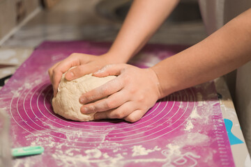 A close-up shot of hands kneading a fresh ball of white dough on a purple silicone baking mat in a kitchen setting.