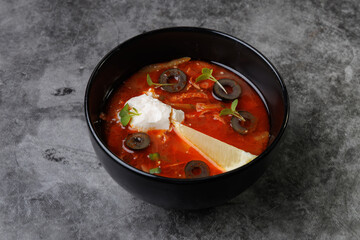 Red Tomato Soup In Black Bowl With Olive Slices, Cream