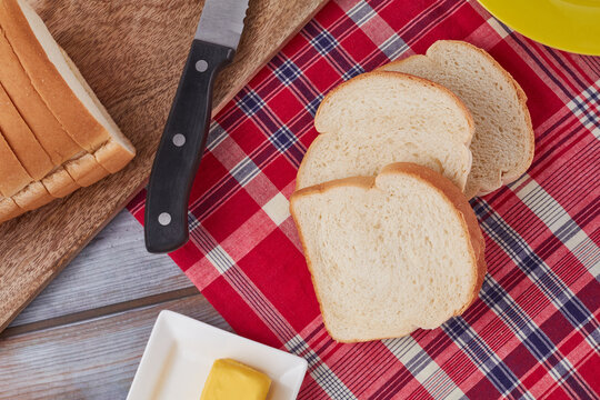 Three (3) slices of Jamaican hard dough bread on a Jamaican bandana with a yellow plate, cutting board, knife and a stick of butter