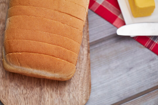 A freshly baked loaf of Jamaican sliced hard dough bread on a cutting board with a stick of butter and a knife