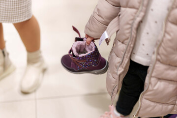Little hands holding new boots while shopping for Winter clothes at the Mall