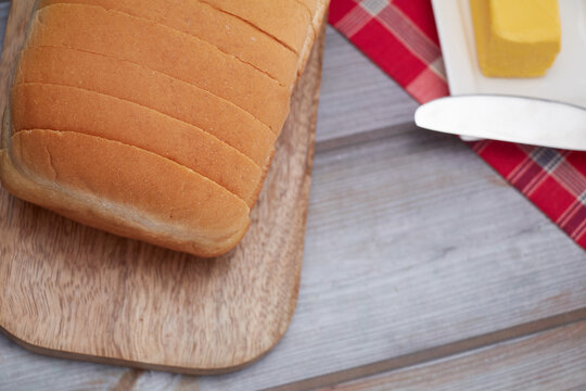 A freshly baked loaf of Jamaican sliced hard dough bread on a cutting board with a stick of butter and a knife