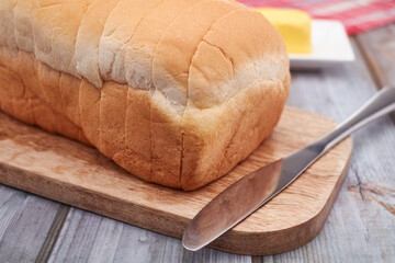 A freshly baked loaf of Jamaican sliced hard dough bread on a cutting board with a stick of butter and a knife