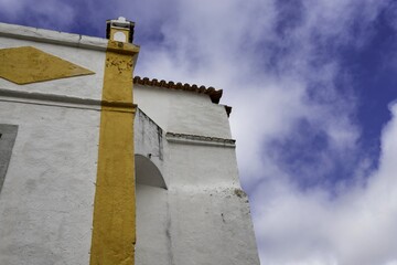 View of a striking white building with vibrant yellow accents reaching towards a blue sky dotted with soft clouds, Obidos, Leiria District, Portugal.