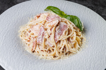Creamy Pasta Carbonara With Bacon and Basil Garnish On White Plate
