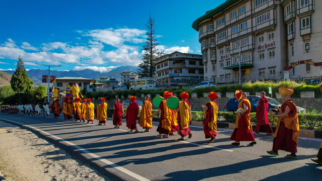 Aerial view of monks in vibrant orange robes walking along a road with long shadows cast against the backdrop of Thimphu buildings, Thimphu, Thimphu, Bhutan.