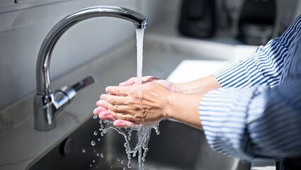 Close-up of a person washing their hands under a running faucet in a kitchen sink, demonstrating hygiene practices
