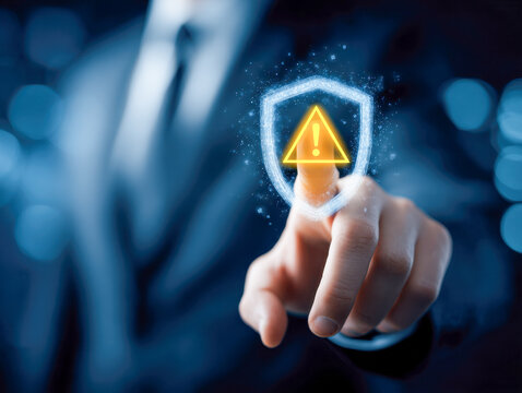 Businessman touching shield icon with warning symbol representing cybersecurity risks and digital threat protection in technology concept background