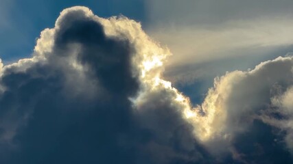 Dramatic detail of cumulous clouds, building and changing, and dark except for a brightly backlit portion and a bright opening to blue sky.