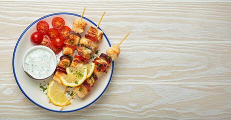 Grilled chicken skewers seasoned with herbs and spices, served on a plate with lemon wedges, cherry...
