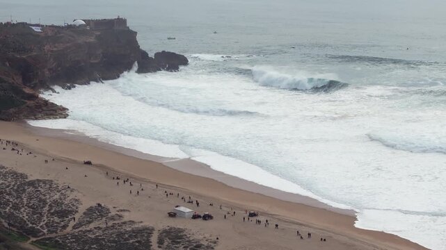 Ultra wide aerial panorama of Nazare extreme big wave surfing competition event with cliff spectators, lighthouse and massive Atlantic swell in Portugal