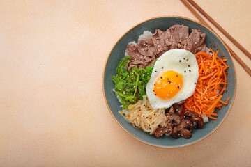 Bibimbap, authentic korean dish with a steamed rice topped with fried egg, beef, colorful vegetables, traditional dish of Korea top view on warm beige background