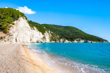Obraz premium Majestic white limestone cliffs towering over a quiet pebble Vignanotica beach on the Gargano coast, Apulia, Italy