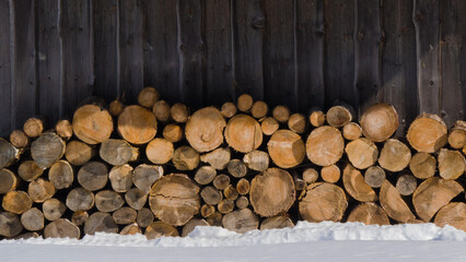 Stacked logs provide warmth and beauty against a rustic wooden backdrop in a winter landscape.