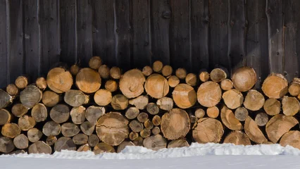 Fotobehang Brandhout Stacked logs provide warmth and beauty against a rustic wooden backdrop in a winter landscape.  © Carterson