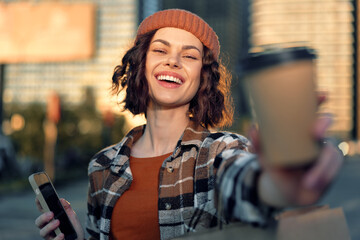 Woman with coffee and smartphone in urban street wearing beanie, smile and golden light, candid authenticity and lifestyle moment with mindful living vibe and emotional storytelling.