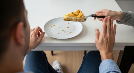 A man makes a stop gesture with his hand to refuse a slice of pie being offered by a woman. An over-the-shoulder view shows his empty plate with crumbs.