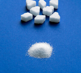 White crystal granulated sugar and sugar piece cubes in blur on blue background.