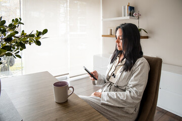 A woman is sitting at a table with a cell phone in her hand