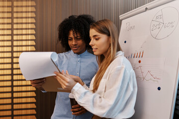 Multiracial coworkers discussing business plan near flipchart in office