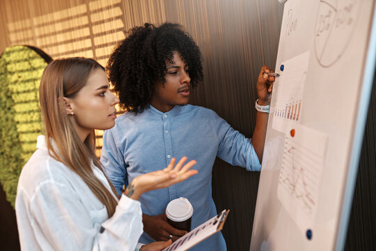 Coworkers discussing data charts on flipchart in modern office