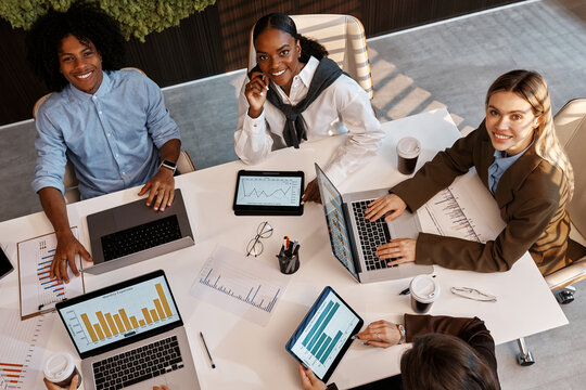 Diverse business team analyzing charts during office meeting from top view