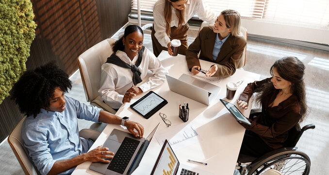 Diverse business team analyzing charts during office meeting from top view